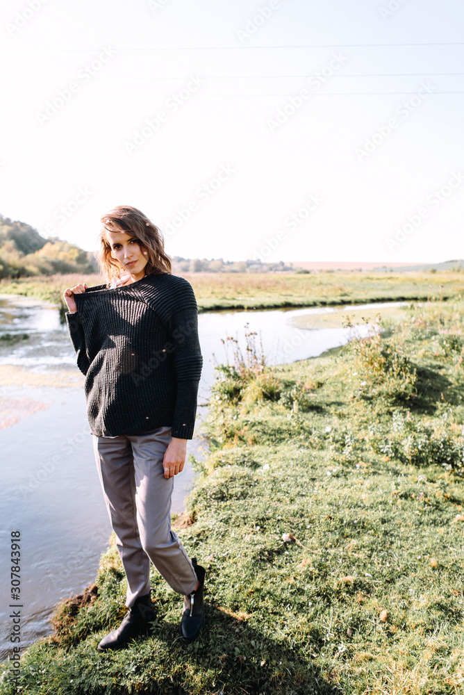 Gentle portrait of beautiful girl or woman in sweater in backlight on river background