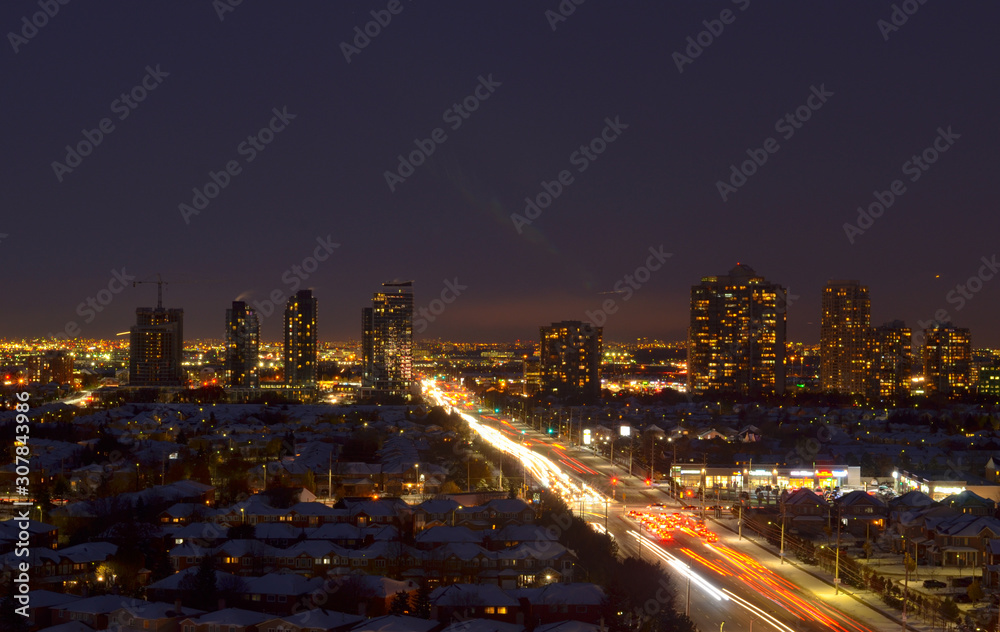 Fototapeta premium Wieczór / noc Widok z Ariel na domy sąsiedzkie w Ameryce Północnej w Mississauga, Ontario, Kanada. Połączone autostradą, w tle widać zgarniacze śródmiejskie