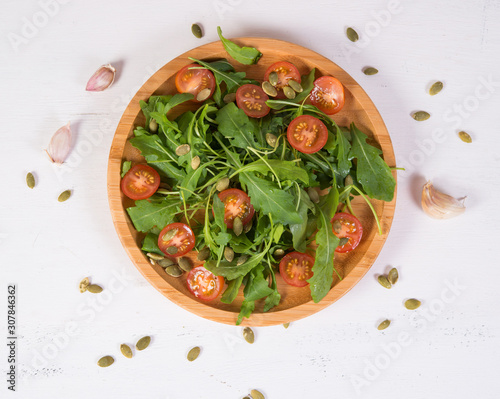 Fresh vegetable salad. Vegetarian salad of arugula, cherry tomatoes and pumpkin seeds in a wooden plate. The concept of pure and natural food. Horizontal photo. Top view
