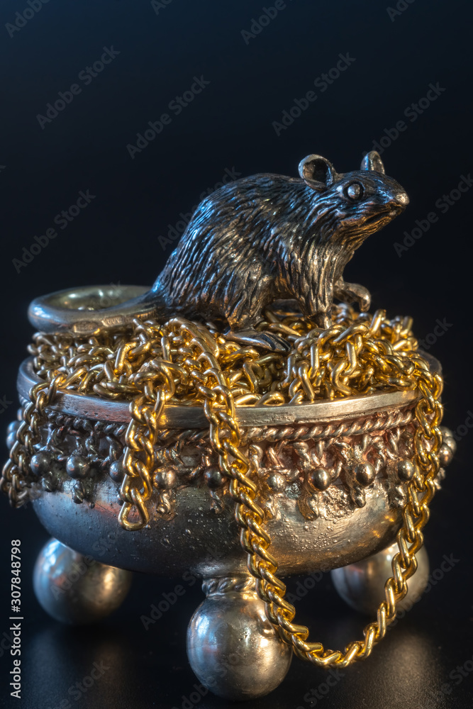 Composition from metal figures: a rat sits in a pot of gold. Products from silver and gold. Concept for the zodiac calendar in 2020. Symbol of well-being and prosperity and wealth. Black background Composition from metal figures: a rat sits in a pot of gold. Products from silver and gold. Concept for the zodiac calendar in 2020. Symbol of well-being and prosperity and wealth. Black background