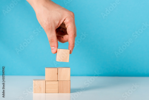 cropped view of man putting wooden cube on blue