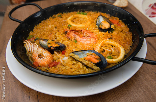 Paella isolated on natural dark background, traditional Spanish food, seafood paella in the fry pan with mussels, king prawns, langoustine and squids. Cooking paella closeup