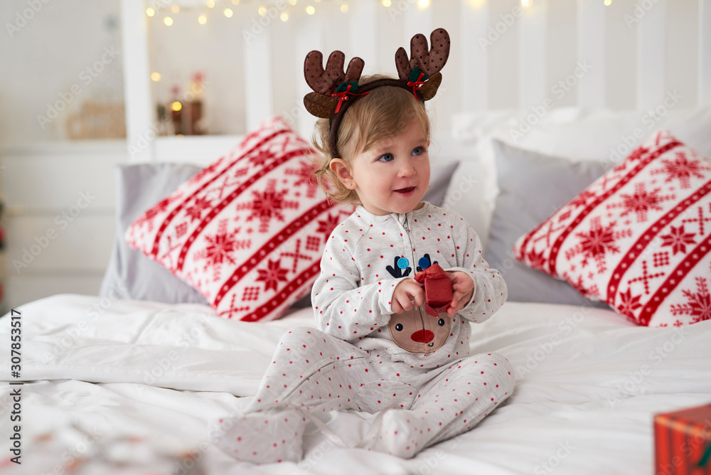 Charming baby opening the Christmas present in bed Charming baby opening the Christmas present in bed