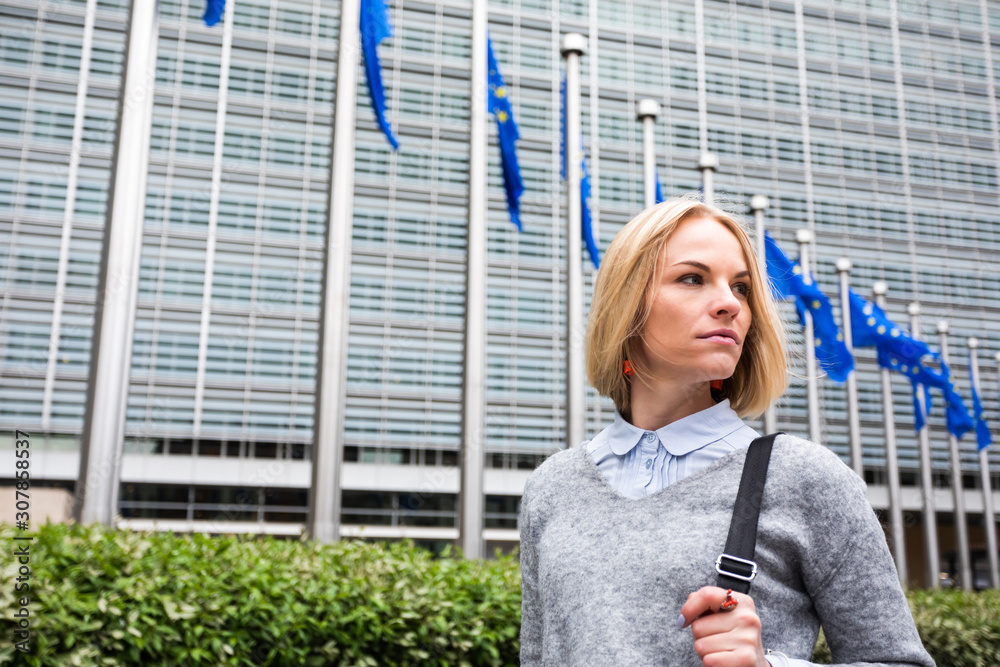 A young woman stands against the backdrop of the European Commission headquarters in Brussels, Belgium