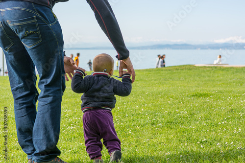 Cute baby girl learning to walk with her father in a park.