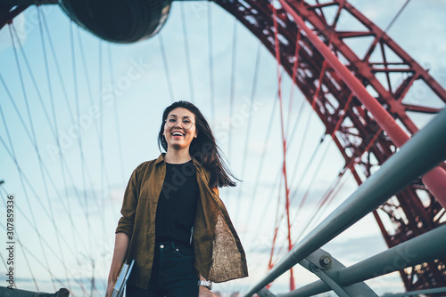 Half length portrait of cheerful asian hipster girl in eyewear enjoying free time walk on urban settings, amazed emotional female student traveler having fun during journey on vacations look at camera #307859336