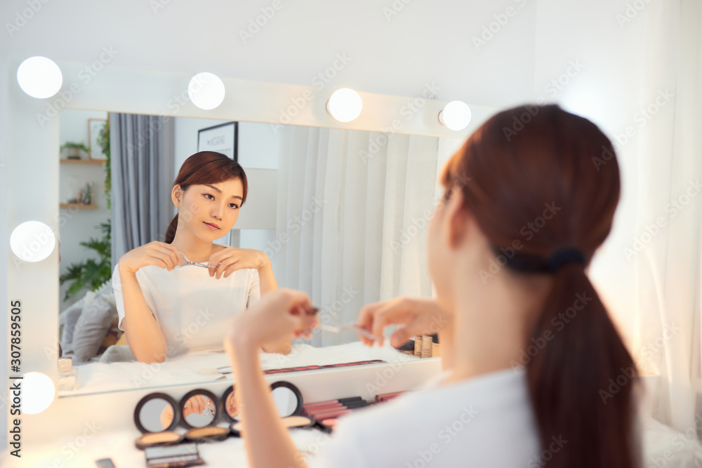 A beautiful Asian girl holding an eyelash curler in her hand as a makeup accessory. A beautiful Asian girl holding an eyelash curler in her hand as a makeup accessory.