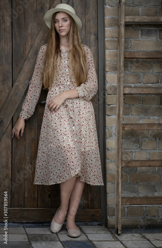 Bored girl in a rustic cotton dress near the door of the barn