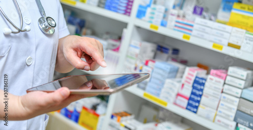 Doctor using computer tablet for search bar on display in pharmacy drugstore shelves background.Online medical concept. photo