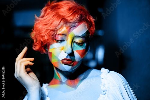 Portrait of a mysterious beautiful woman in blue night lighting with red coral hair and multi-color makeup. Festive futuristic concept of New Year party. Bright color funny mood. Selective focus
