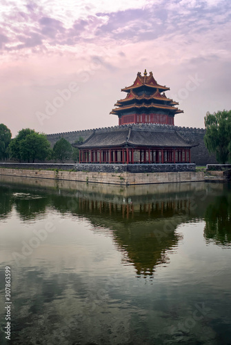 Corner Tower of Forbidden City under the outer Moat at dusk. tower and trees are reflected in the water