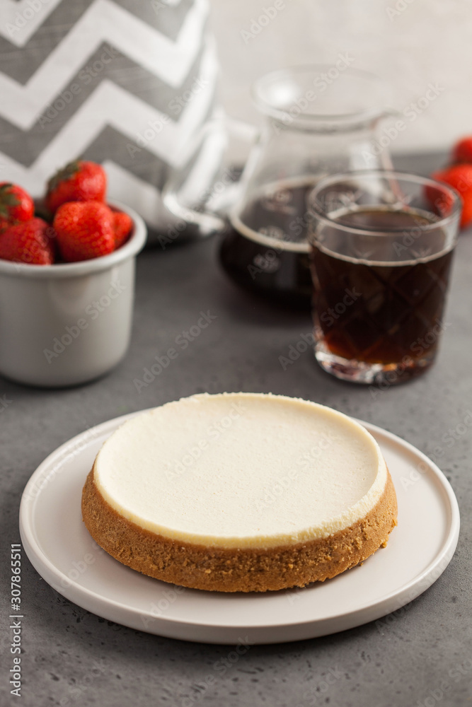 Coconut cheesecake on a round plate. In the background, a teapot with black coffee and a mug of fresh strawberries. Food photo on gray background. Coconut cheesecake on a round plate. In the background, a teapot with black coffee and a mug of fresh strawberries. Food photo on gray background.
