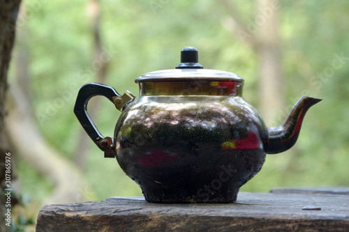 Teapot on wood fire at the camping site . old, dirty, iron kettle on the table