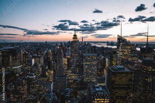 Aerial view of skyscrapers and towers in midtown skyline of Manhattan with evening sunset sky. Scenery cityscape of financial district with famous New York Landmark  illuminated Empire State Building