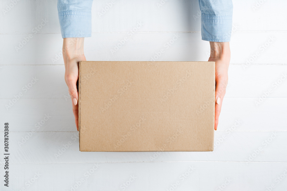 Rectangular cardboard box in female hands. Top view, white background - obrazy, fototapety, plakaty 