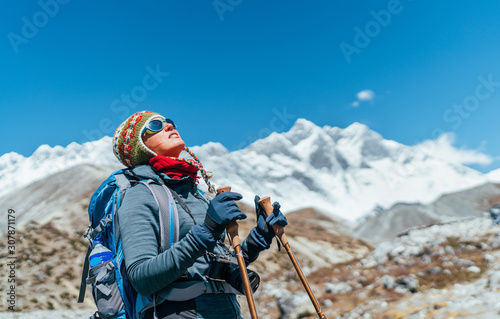 Young hiker backpacker female taking brake in hike walking during high altitude Everest Base Camp (EBC) route with snow Himalayan peaks on background.She using trekking poles. Active vacations concept