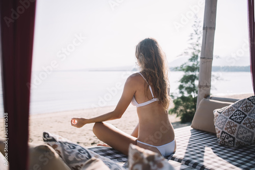 Woman sitting on beach bed and relaxing in lotus position © BullRun