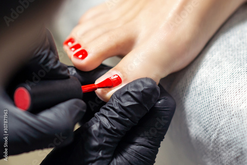 Tableau sur toile Woman receiving red nail polish on fingers of feet close up.