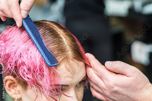 Male hairdresser is combing pink hair of young woman close up in hair salon.