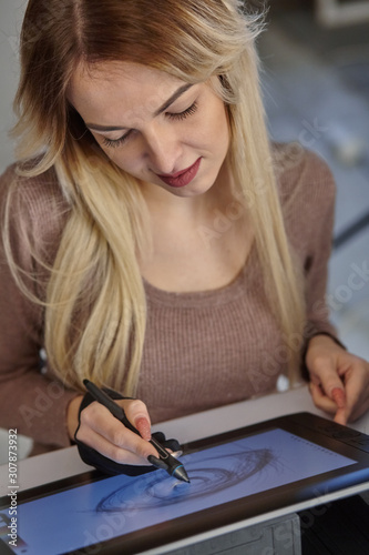 girl artist draws a digital pen on a professional tablet in her studio