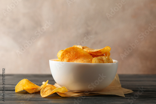Potato chips in a bowl, craft paper on wooden table against brown background, space for text