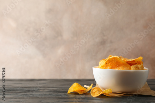 Potato chips in a bowl, craft paper on wooden table against brown background, space for text