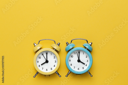 Two round alarm clocks yellow and blue on the yellow background.