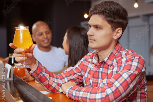 Young handsome man enjoying his beer at the local pub. Attractive man examining beer in his glass before drinking