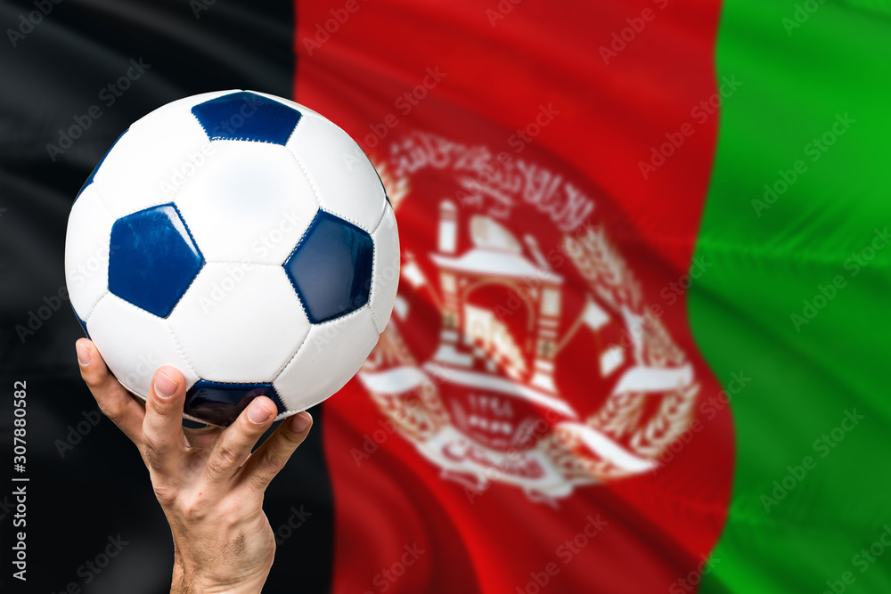 Naklejka premium Afghanistan soccer concept. National team player hand holding soccer ball with country flag background. Copy space for text.