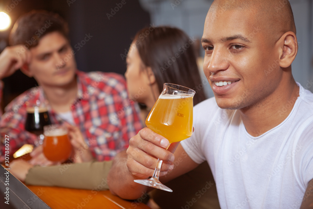 Close up of a handsome African man smiling joyfully, drinking beer at the pub