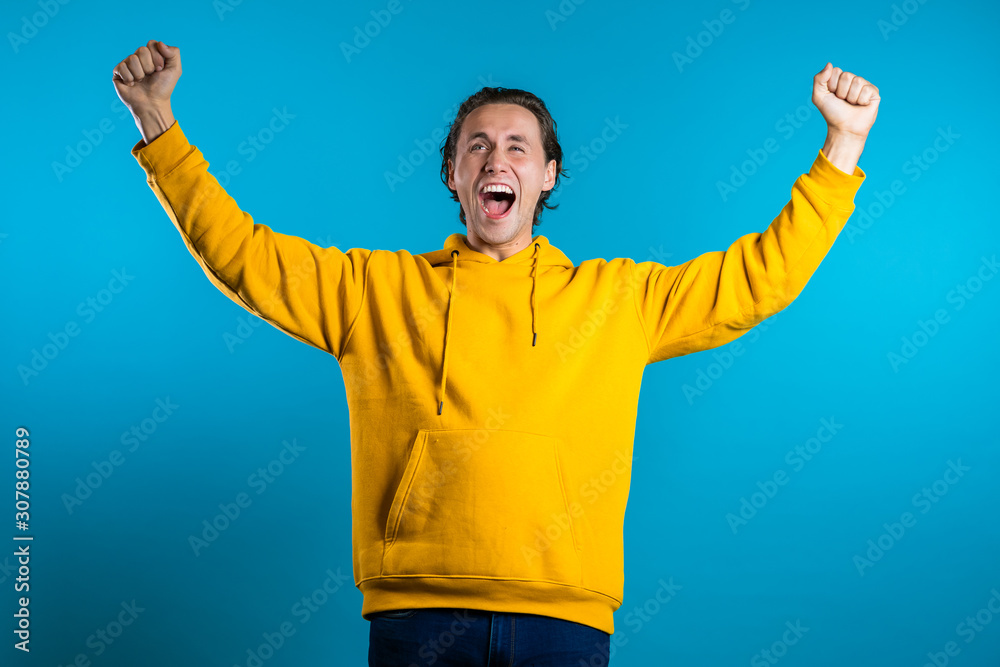 Fototapeta premium Yes winner gesture. Happy european man. Handsome guy with stylish hairdo surprised to camera over blue background