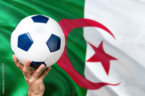 Algeria soccer concept. National team player hand holding soccer ball with country flag background. Copy space for text.