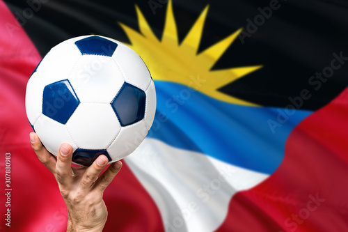 Antigua and Barbuda soccer concept. National team player hand holding soccer ball with country flag background. Copy space for text.