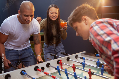 Beautiful young Asian woman cheering her friends during table football match. Happy friends playing table soccer at beer pub