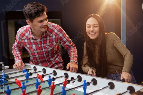 Beautiful happy Asian woman laughing, playing table football with her boyfriend