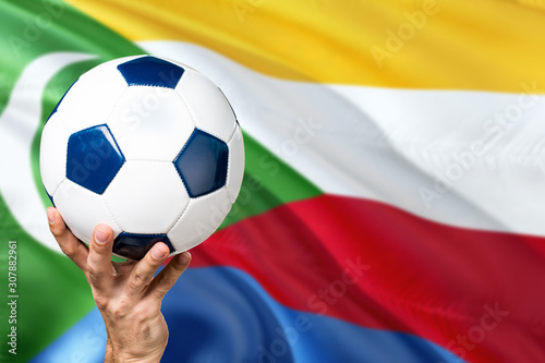 Comoros soccer concept. National team player hand holding soccer ball with country flag background. Copy space for text.