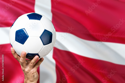 Denmark soccer concept. National team player hand holding soccer ball with country flag background. Copy space for text.