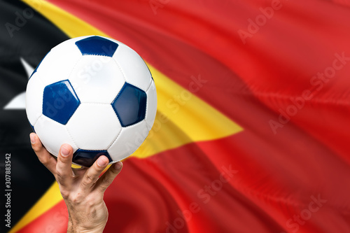 East Timor soccer concept. National team player hand holding soccer ball with country flag background. Copy space for text.