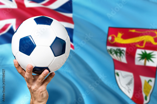 Fiji soccer concept. National team player hand holding soccer ball with country flag background. Copy space for text.