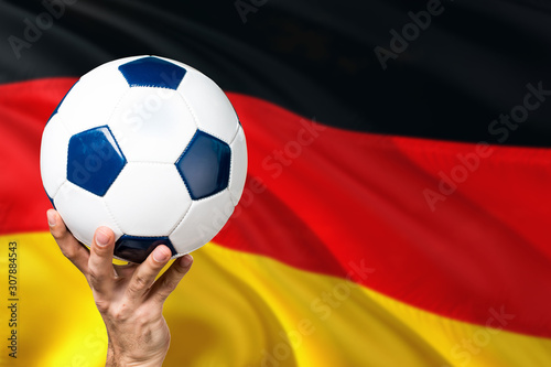 Germany soccer concept. National team player hand holding soccer ball with country flag background. Copy space for text.