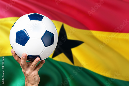 Ghana soccer concept. National team player hand holding soccer ball with country flag background. Copy space for text.