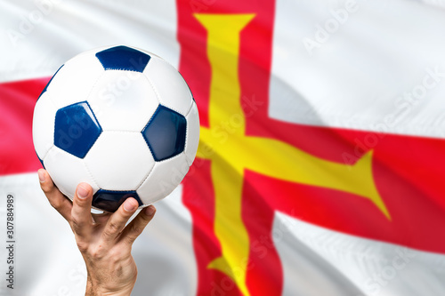 Guernsey soccer concept. National team player hand holding soccer ball with country flag background. Copy space for text.