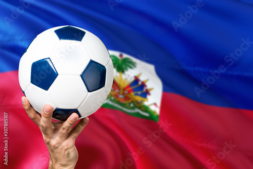 Haiti soccer concept. National team player hand holding soccer ball with country flag background. Copy space for text.