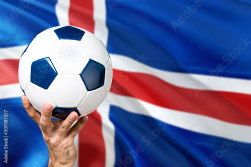Iceland soccer concept. National team player hand holding soccer ball with country flag background. Copy space for text.