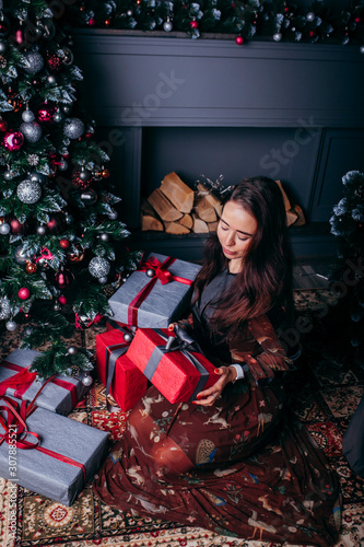Portrait of young smiling model woman in decorated living room with gifts and Christmas tree
