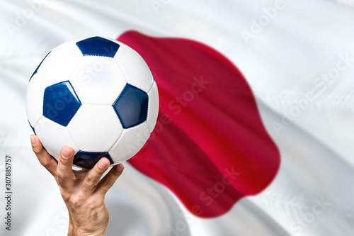 Japan soccer concept. National team player hand holding soccer ball with country flag background. Copy space for text.