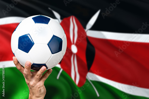 Kenya soccer concept. National team player hand holding soccer ball with country flag background. Copy space for text.