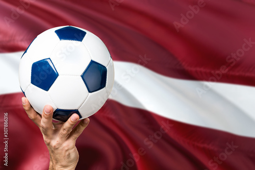 Latvia soccer concept. National team player hand holding soccer ball with country flag background. Copy space for text.