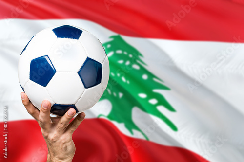 Lebanon soccer concept. National team player hand holding soccer ball with country flag background. Copy space for text.