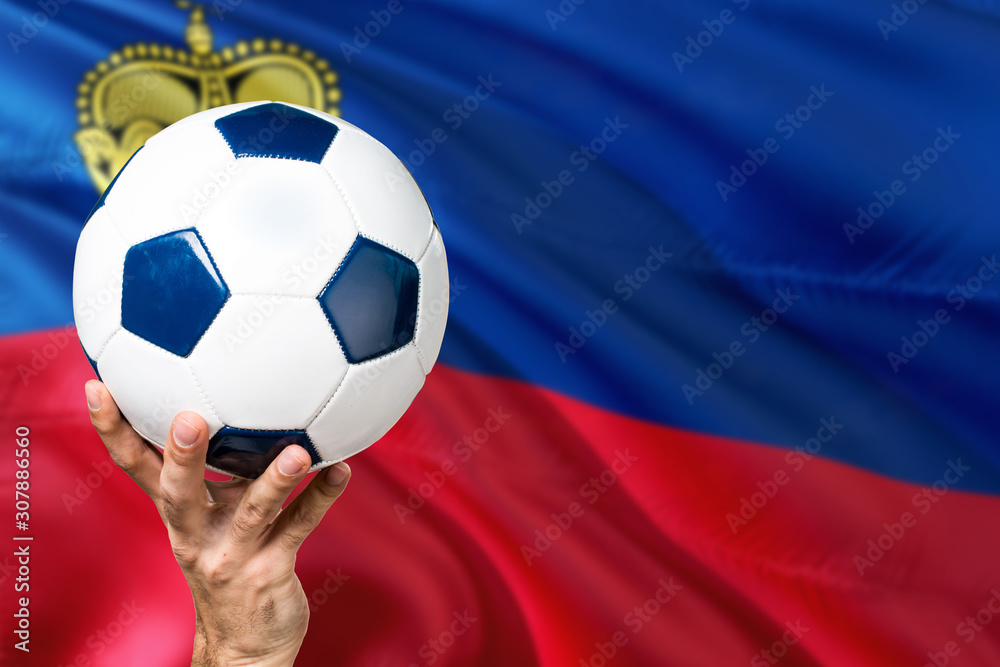 Naklejka premium Liechtenstein soccer concept. National team player hand holding soccer ball with country flag background. Copy space for text.